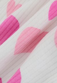 Biały materiał o prążkowanej fakturze z dużymi różowymi i jasnoróżowymi wzorami serc. Zbliżenie podkreśla miękkość i kontrast kolorów.