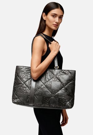 Borsa tote nera trapuntata con motivo logo, dotata di una tracolla in pelle liscia e di un design spazioso e strutturato, tenuta da una modella.