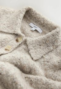 Svetlobežový, textúrovaný sveter s golierom, dvoma veľkými gombíkmi a tkaným vzorom; štítok hovorí "NEXT."