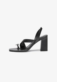 Sorte læder højhælede sandaler med flad sål, der har krydsede stropper, en rund metallisk detalje og en solid blokhælk.