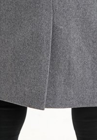 Cappotto grigio in feltro con taglio dritto e cucitura centrale. La texture è morbida e leggermente pelosa, progettata per fornire calore.
