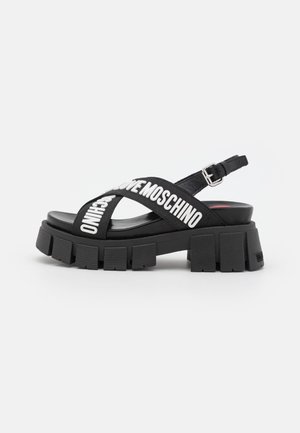 Sort platform-sandal med kraftig rillesål, justerbar bagrem og krydsede stofbånd med hvid "LOVE MOSCHINO" tekst.