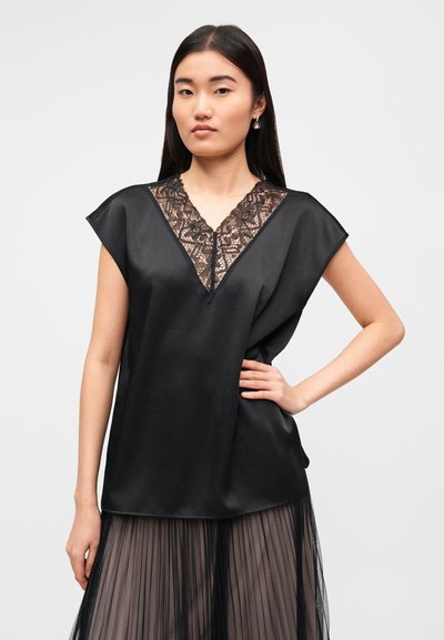 Μαύρο σατέν τοπ με κοντά μανίκια, ντεκολτέ σε σχήμα V και δαντελένιες λεπτομέρειες στον γιακά. Το μοντέλο φοράει πλισέ, διαφανής φούστα σε αντίθετο χρώμα.