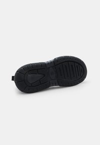 Suela de zapato de goma negra con un dibujo texturizado, que presenta un diseño de soporte central y una pequeña lengüeta en el talón.