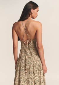 Maksimalios ilgio suknelė su smėlio spalvos gėlių raštu, reguliuojamomis kryžminėmis petnešėlėmis ir surišama detalė nugaroje. Lengva medžiaga su laisvai krintančia forma.