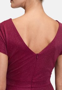 Burgunderfarbene Kleid mit V- Rücken, kurzen Ärmeln und Reißverschluss. Der Stoff hat einen dezenten Glanz und eine glatte Textur.