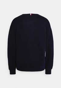 Pull en maille bleu marine foncé à manches longues avec un petit détail en tissu rouge, blanc et noir au niveau du col arrière.