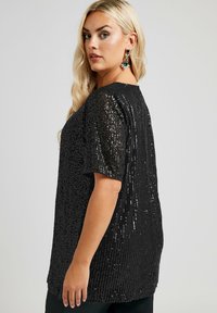 Svart paljett-topp med korta ärmar, med ett strukturerat mönster och lös passform. Slät, blank yta som reflekterar ljus.