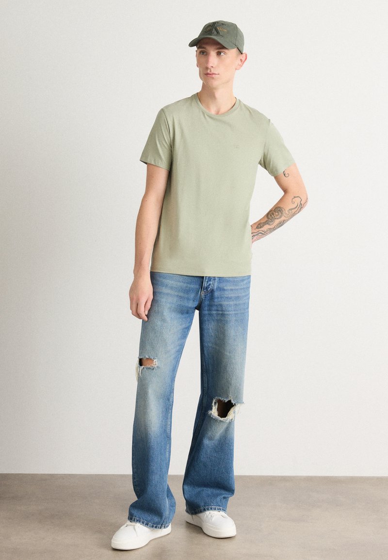 Olive green t-shirt with a crew neck, paired with light blue distressed jeans featuring torn knees, and white sneakers for footwear.