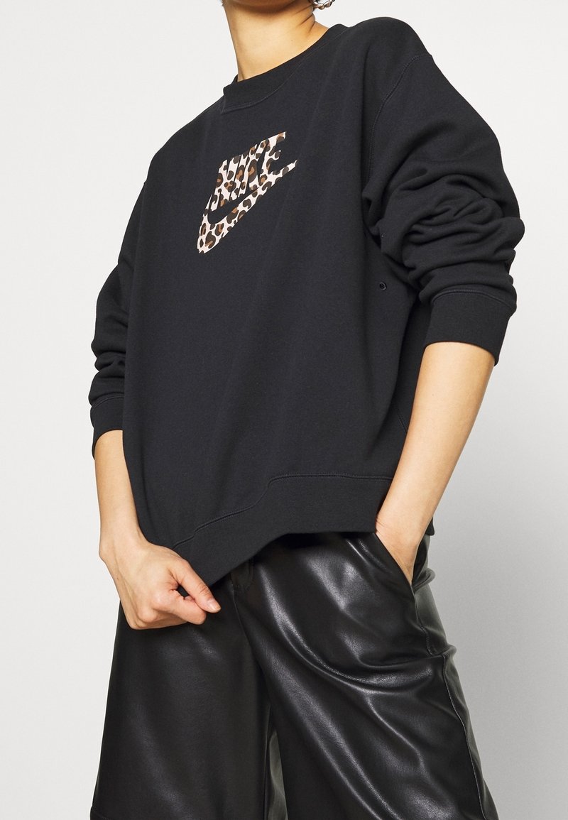 Zwarte sweatshirt met een leopardprint Nike-logo. Heeft een relaxte pasvorm, ronde halslijn en ribgebreide boorden. Gestyleerd met zwarte leren shorts.