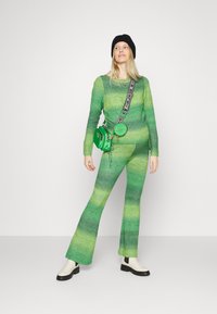 Conjunto de malha em gradiente verde, com uma blusa de manga longa e calças abertas. Acentuado com um gorro preto e uma bolsa de ombro verde. Botas de salto baixo.