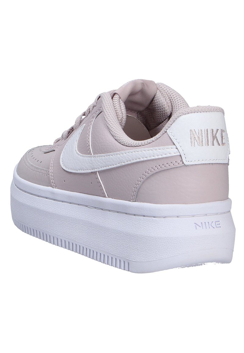 Sneaker Nike in pelle rosa chiaro con accenti bianchi, dotati di una suola piatta e superficie testurizzata. I lacci sono visibili nella parte anteriore.