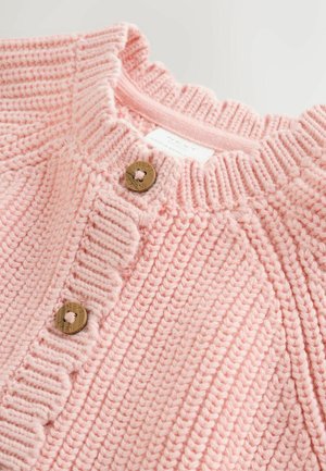 Light pink knitted cardigan with a scalloped collar, featuring two round brown buttons and a label, textured fabric in a ribbed pattern.