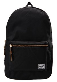 Sac à dos en tissu noir avec poche avant zippée, tirettes en cuir et étiquette de marque rectangulaire blanche sur le coin de la poche.