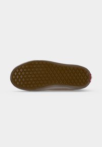 Semelle de chaussure en caoutchouc marron avec un motif de rainure en forme de gaufre et de points, vue par le dessous sur fond blanc.