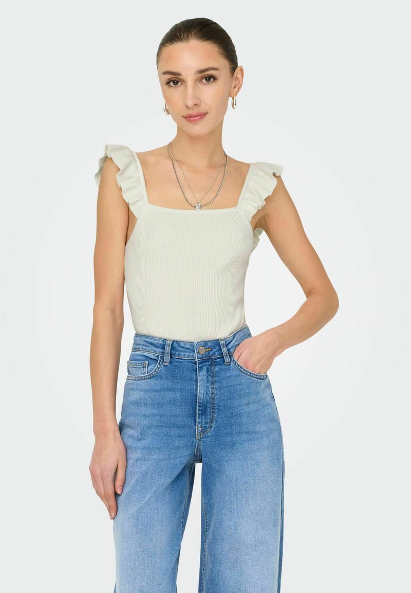 Lys grøn ribbet tanktop med volanger på ærmerne, parret med højtaljede lyseblå bredde jeans. Enkle sølv smykkedetaljer.