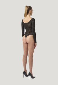 Sort langærmet bodysuit med et leopardmønster, der har åben ryg og højudskårne ben. Matchet med sorte høje hæle.