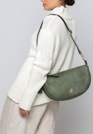 Grüne Wildleder-Handtasche mit geschwungener Form, ausgestattet mit einem schwarzen Trageriemen und einem goldenen Logo-Akzent. Die Textur wirkt weich und glatt.