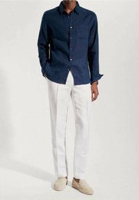 Chemise bleu marine à boutons, manches longues, associée à un pantalon en lin blanc et des espadrilles beiges. Elle dispose d'une poche poitrine et d'une coupe décontractée.