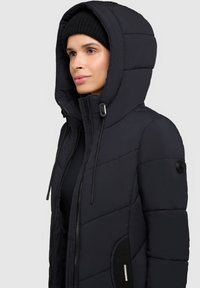 Vatteret jakke i mørk marineblå, med lynlås foran, høj krave, justerbar hætte og sidelommer med elastiske detaljer.