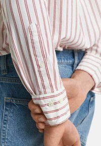 Witte lange mouwen shirt met rode strepen, met knoopmanchetten en geborduurd logo. Heeft een relaxte pasvorm en zachte katoen stof. Draagt met denim.