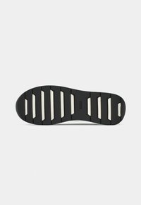 Sole di scarpa in gomma nera con un design segmentato. Presenta accenti bianchi e scanalature visibili per trazione e stabilità.