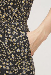 Czarna tkanina w mały biały i żółty wzór kwiatowy, z kieszenią po lewej stronie i marszczeniem w talii.