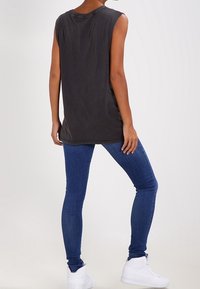 Black sleeveless top with a relaxed fit, paired with blue skinny jeans and white sneakers, viewed from the back. Features a round neckline.