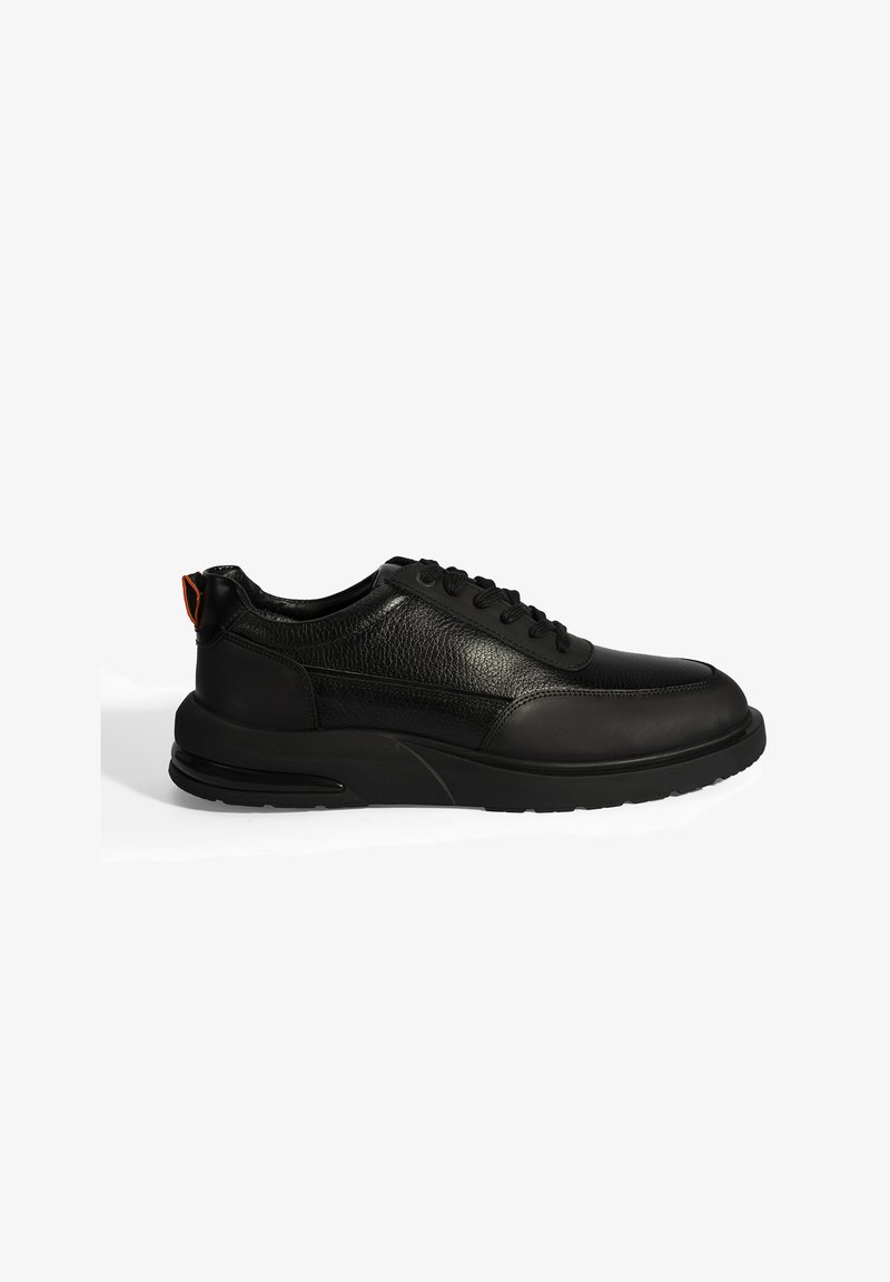 Baskets noires en cuir texturé avec un bout lisse, semelle en caoutchouc et lacets noirs. Dotées d'une languette orange contrastante au niveau du talon.