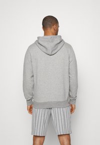 Sudadera con capucha gris de corte relajado, fabricada con un tejido texturizado, con un bolsillo canguro y puños acanalados, combinada con pantalones cortos a rayas.