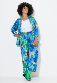 Blauw en groen gestreept outfit met abstracte gezichten, bestaande uit een lange mouwen jas en wijde broek. Gecombineerd met glanzende groene laarzen.