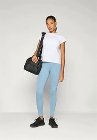 Fekete kézitáska, fehér póló, világoskék leggings és fekete cipő egy álló figurán. A hangsúly a laza sportos öltözködésen és kiegészítőkön van.