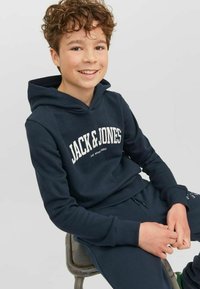 Sudadera navy con el logotipo blanco "JACK & JONES" en el frente, que presenta un bolsillo tipo canguro y puños acanalados. Combinada con pantalones de chándal navy a juego.