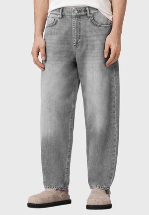 Løse grå denimjeans båret med beige perforerede slip-on sko og en indstukket hvid skjorte.