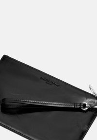 Clutch da polso in pelle nera con logo in rilievo "Liebeskind Berlin" e zip argentata su uno sfondo chiaro.