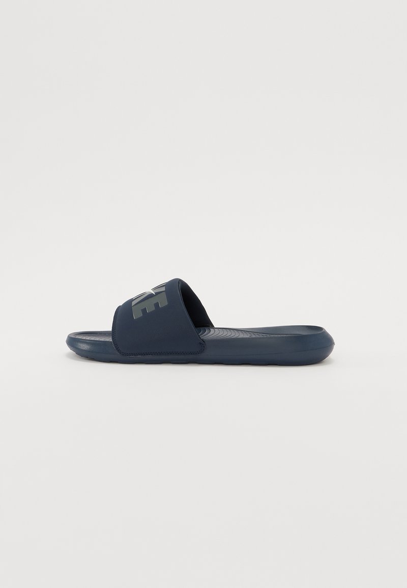 Sandale cu toc de culoare albastru marin, cu o talpă texturată și o curea largă care include un logo contrastant. Fabricate din material sintetic, concepute pentru confort.