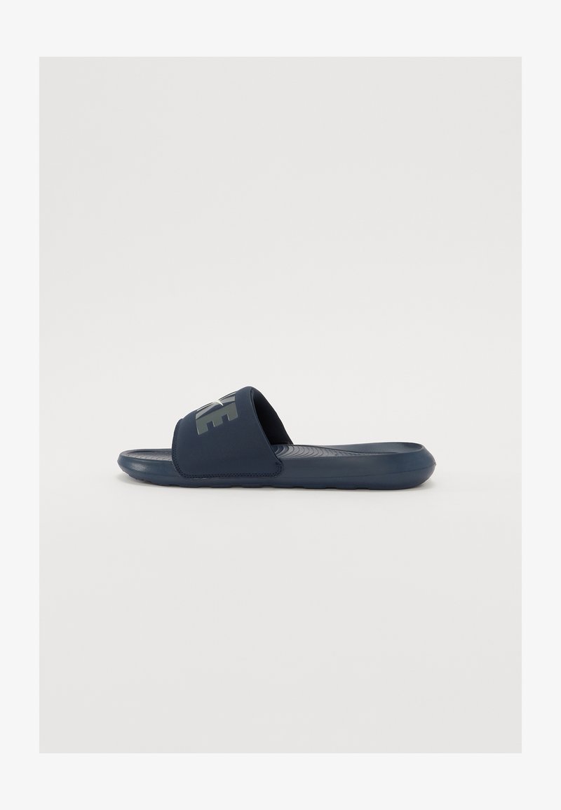 Sandale cu toc de culoare albastru marin, cu o talpă texturată și o curea largă care include un logo contrastant. Fabricate din material sintetic, concepute pentru confort.