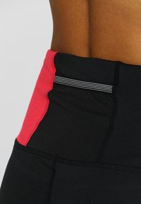 Leggings neri a vita alta con pannello laterale rosa, texture liscia e un dettaglio a strisce bianche in vita.