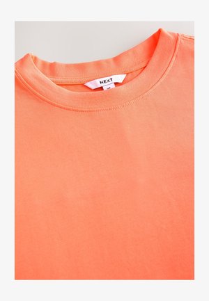 T-shirt a maniche corte in corallo acceso, realizzata in cotone morbido. Presenta una scollatura tonda e un'etichetta cucita con la scritta "NEXT." Texture liscia.