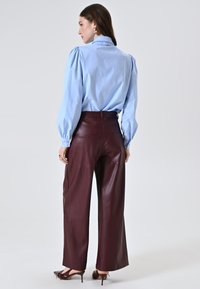 Camicia blusa azzurro chiaro con maniche a sbuffo, abbinata a pantaloni larghi in pelle bordeaux; texture elegante e vestibilità su misura.