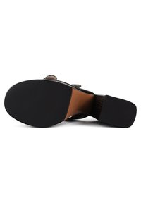 Vue de la semelle d'une chaussure noire à talon avec une semelle avant en caoutchouc texturé et un talon carré sur fond blanc.