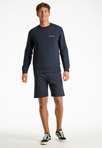 Mörkblå tröja och shorts-set i bomull. Tröjan har ribbat avslut vid ärmar och halslinning, shortsen har resårmidja och logotypdetalj.