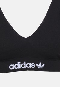 Svart sport-bh med V-halsdesign, med ett brett elastiskt band som har vit "adidas"-logotyp och treflod logotyp. Strukturerad tyg.