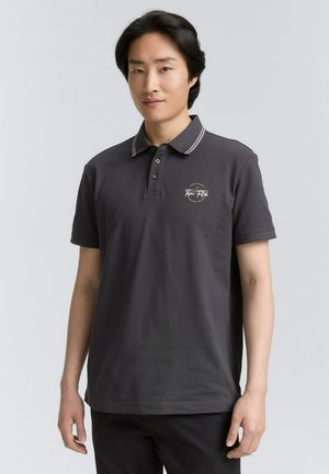 Donkergrijze polo met een kraag met crèmekleurige strepen en een klein geborduurd logo op de borst, gemaakt van katoen.