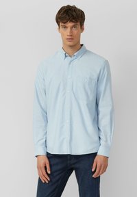 Chemise bleu clair à boutons, fabriquée en tissu doux. Elle comprend un col, des manches longues et une poche poitrine simple avec peu de détails.