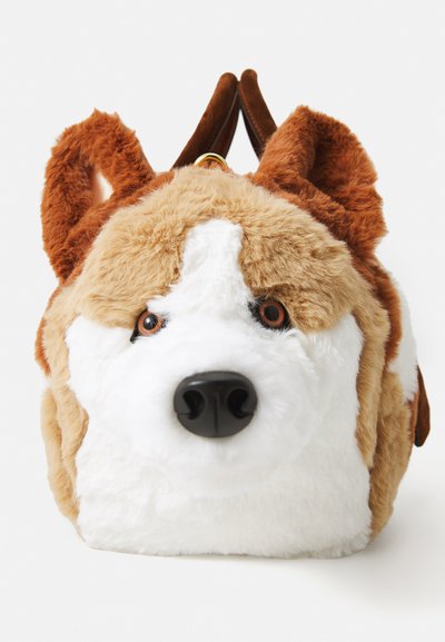 Zaino a forma di cane in peluche con pelliccia marrone, bianca e beige, occhi e naso dettagliati, e spallacci in suede marrone su uno sfondo bianco.