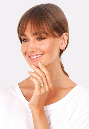 Goldring mit runder Oberkante und gedrehter Bandgestaltung. Model trägt ein weißes Shirt und präsentiert den Ring an ihrer rechten Hand.