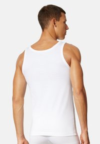 Hvid bomulds tanktop med rund hals, brede stropper og en tætsiddende design, der fremhæver en glat tekstur og minimale sammensyninger.