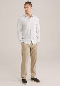 Camisa de botones gris claro de tela de lino, combinada con pantalones beige y alpargatas negras. La camisa tiene un cuello puntiagudo y mangas largas.