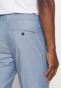 Pantalons à motifs bleu clair avec une poche arrière dotée d'un bouton noir et d'une petite bande d'accent tricolore près de l'ouverture de la poche.
